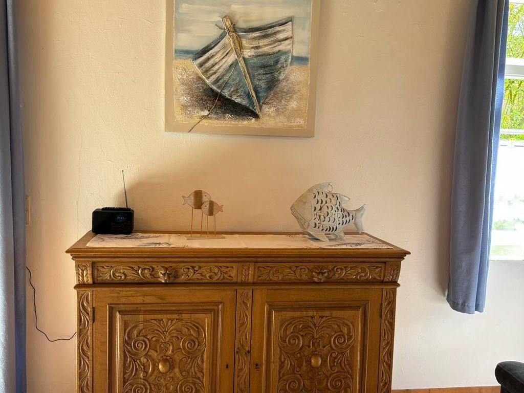 Rustikale Holzkommode mit kunstvollen Schnitzereien, maritimer Deko und Boots-Wandbild in einem gemütlichen Ferienhaus.