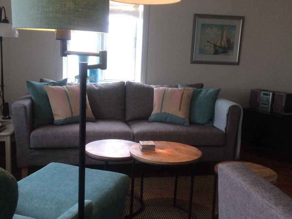 Das helle Wohnzimmer mit vier Fenstern ist ausgestattet mit einem Sofa und zwei Sesseln.