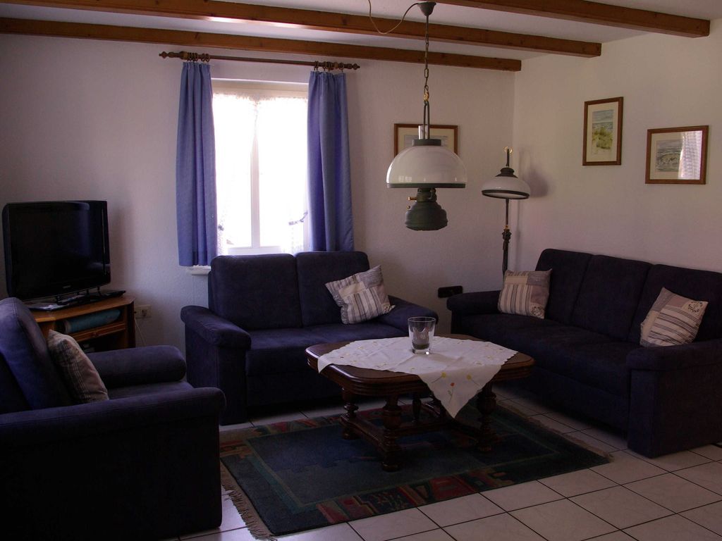 Gemütliches Wohnzimmer im Ferienhaus mit einladender Sitzgruppe, TV und rustikalen Deckenbalken für entspannten Urlaub.