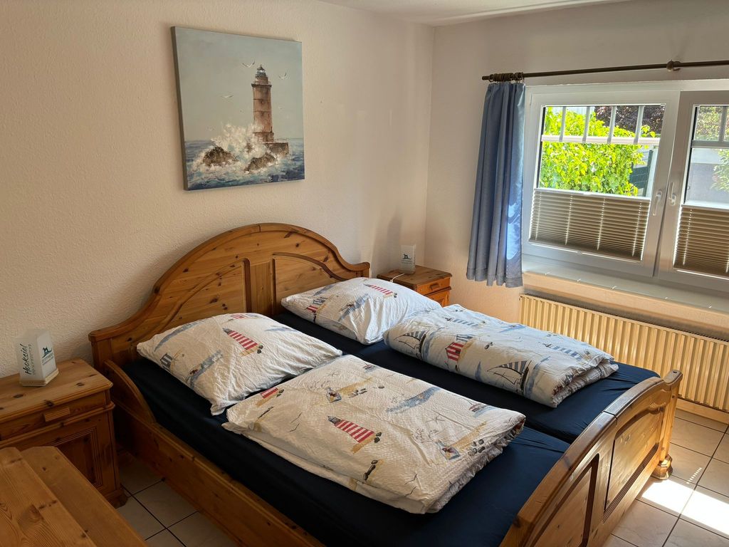 Schlafzimmer EG. Helles Schlafzimmer im Ferienhaus mit gemütlichem Doppelbett, maritimer Bettwäsche und Leuchtturm-Bild für erholsame Nächte.