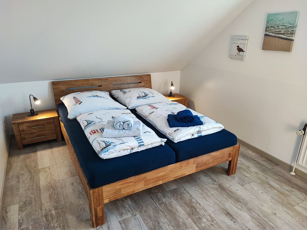 Doppelbettzimmer 1.OG Gemütliches Ferienhaus-Schlafzimmer unter einer Dachschräge mit Massivholz-Doppelbett, maritimer Bettwäsche und Nachttischen.
