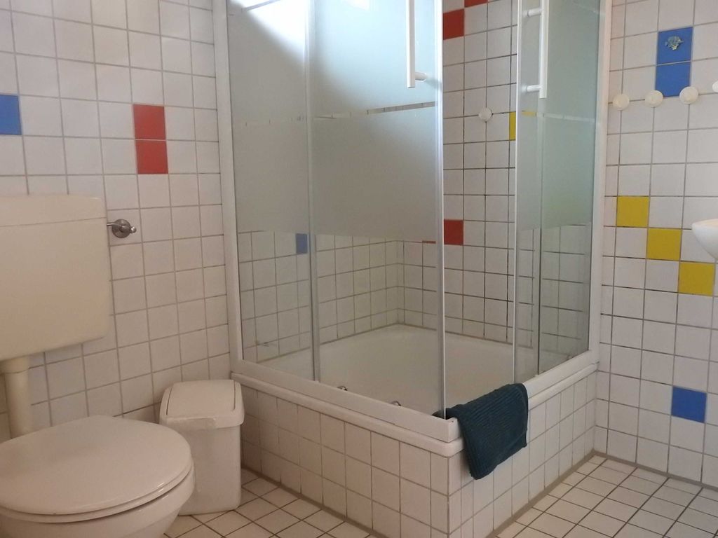 Bad mit Dusche im EG Hell gefliestes Badezimmer im Ferienhaus mit WC, Mülleimer und einer Eckduschkabine mit Milchglaselementen und bunten Fliesenakzenten.