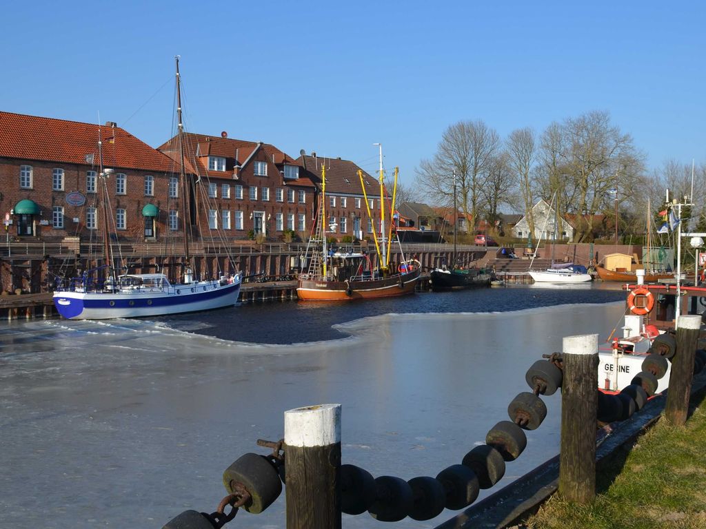 Hafen von Hooksiel Wo das Eis noch bleibt und die Segel schon vom Sommer träumen: Historischer Hafen mit Backsteinfassaden, festgemachten Traditionsschiffen und glitzerndem Winterlicht unter wolkenlosem Himmel.
