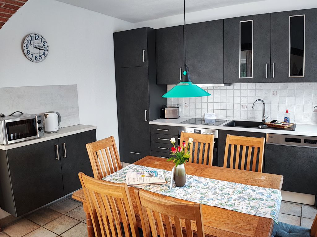 Küche Gemütlicher Essbereich und moderne Küche einer Ferienwohnung mit Holztisch, dunkelgrauen Schränken und maritimem Wandflaschendesign.