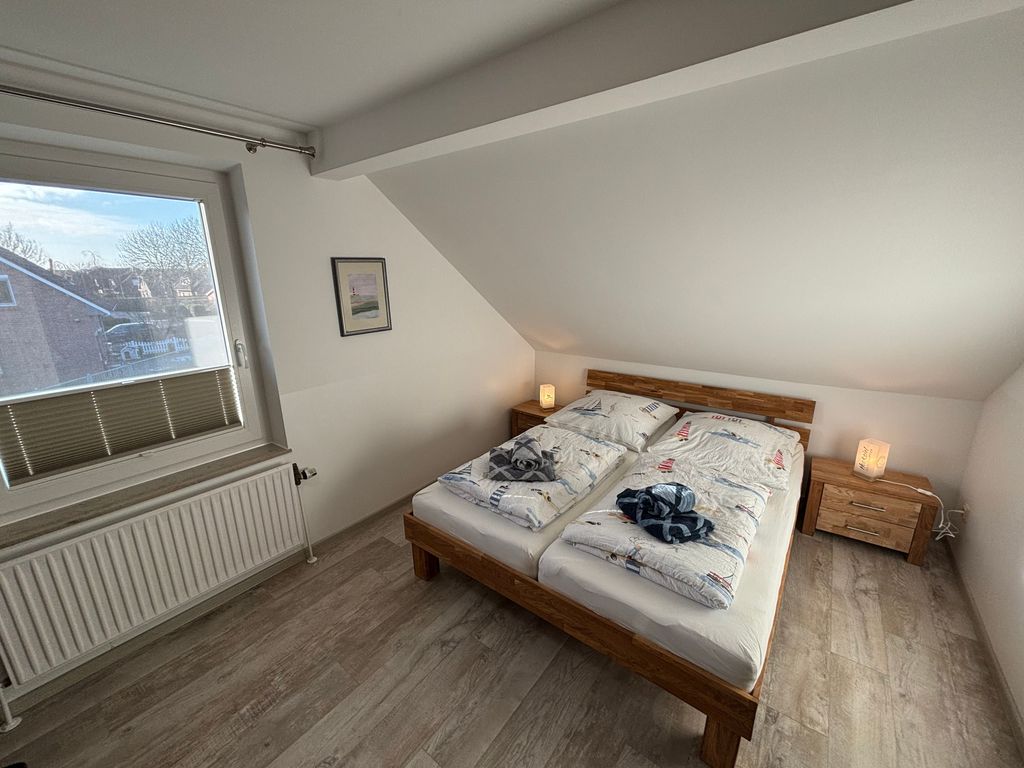 Schlafzimmer Doppelbett 1.OG Helles Schlafzimmer im Ferienhaus mit Doppelbett aus Massivholz, maritimer Bettwäsche, Nachttischen und einem großen Fenster unter einer Dachschräge.