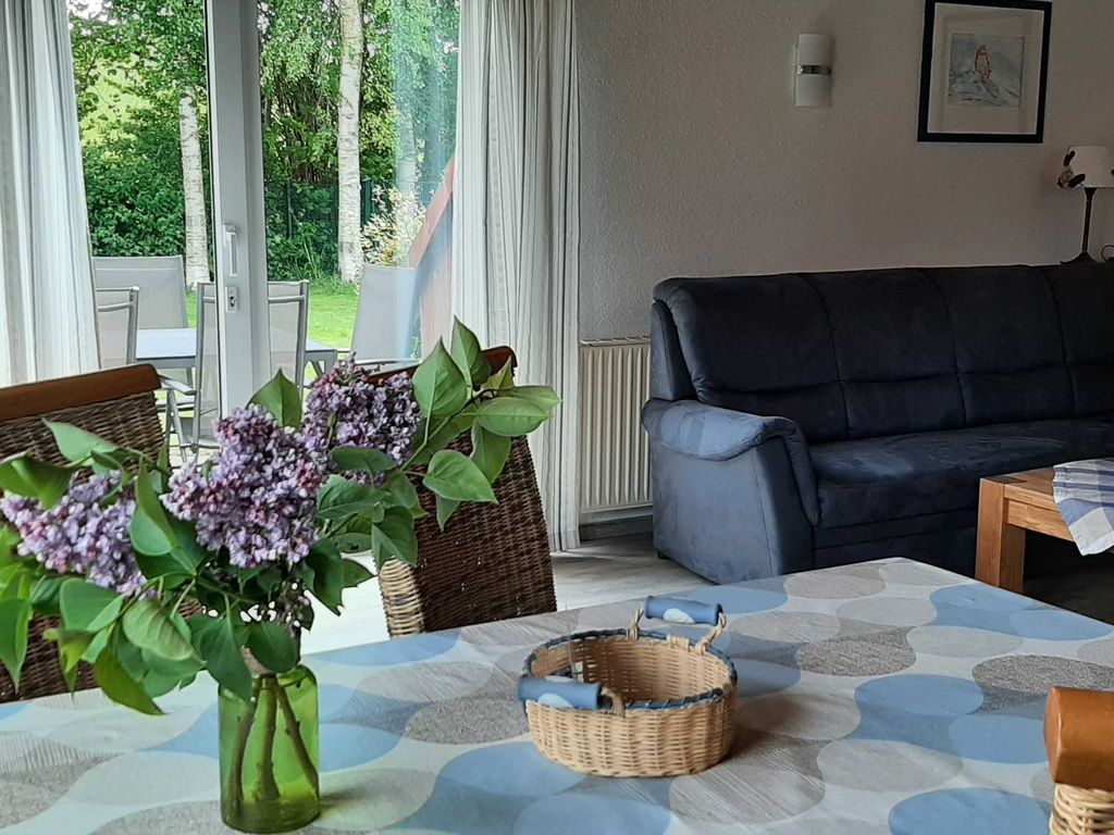 Blick in den Garten Helles Wohnzimmer im Ferienhaus mit gemütlichem Ecksofa, Esstisch im Vordergrund und großen Terrassentüren zum grünen Garten.