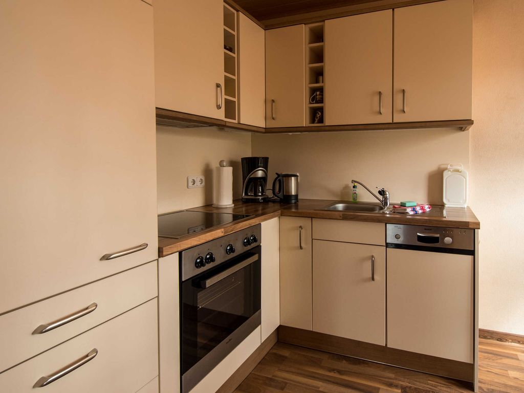 Die Küche als abgeschlossener Raum mit Kühlschrank mit einem Tiefkühlfach, Ceranfeld, Backofen und Geschirrspüler. Ein Tisch mit zwei Stühlen bietet Platz zum Frühstücken.