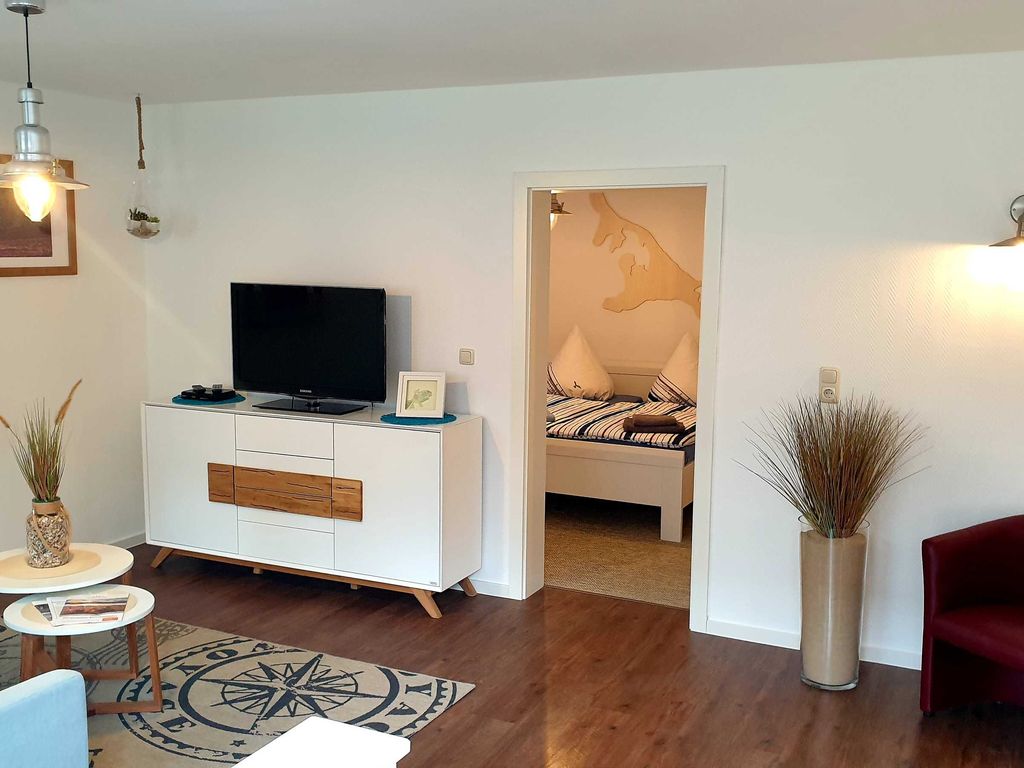 Blick vom Wohnraum mit Couch, Flach-TV und Leseecke in das Schlafzimmer