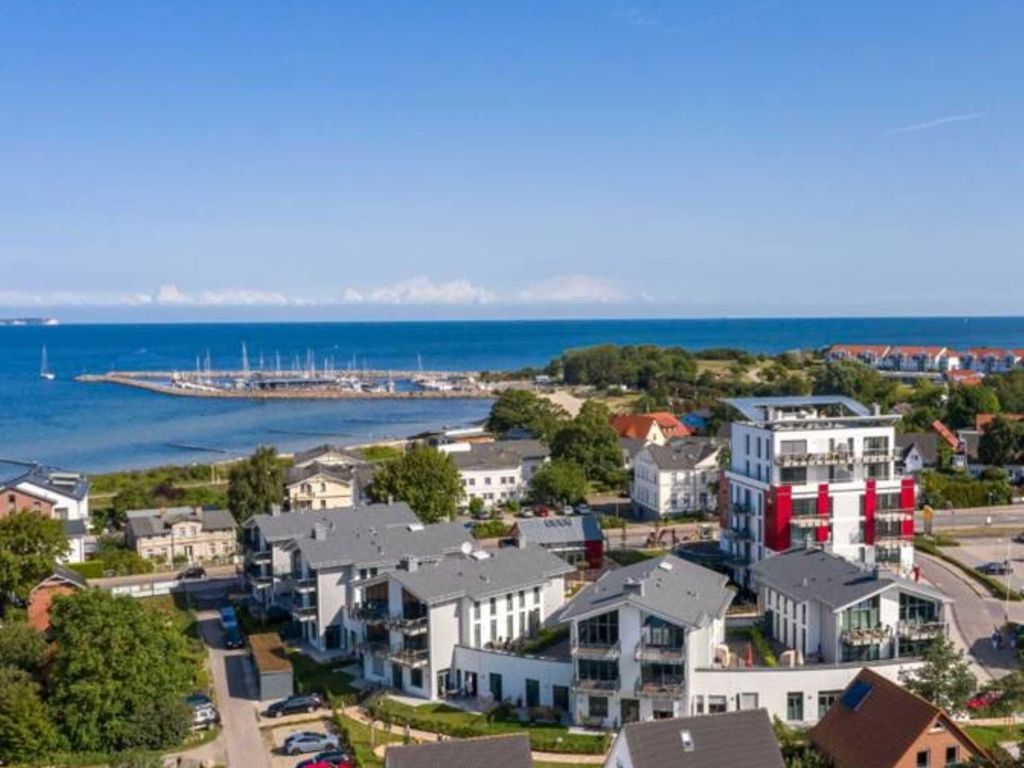 Haus Bodden-Markt Glowe aus der Luft: die weißen Neubauten mit roten Akzenten, dahinter Sportboothafen und Ostsee