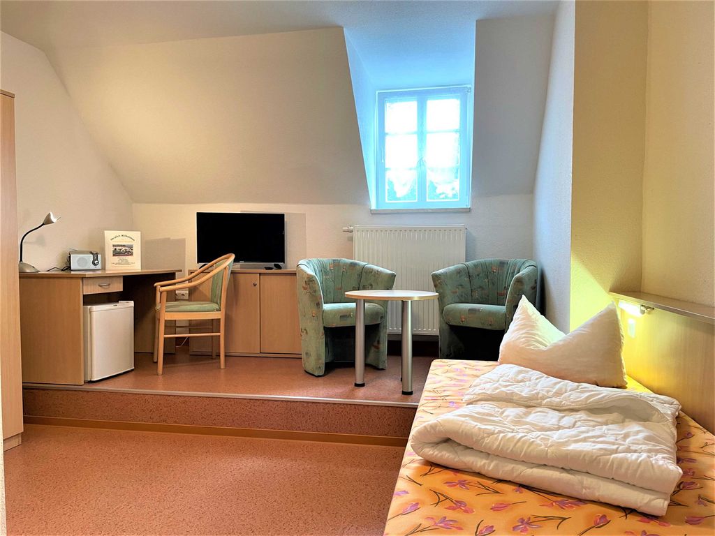 Blick zur gemütlichen Sitzecke mit Sessel, Tischchen, Fernseher,  Schreibtisch und kleinem Kühlschrank