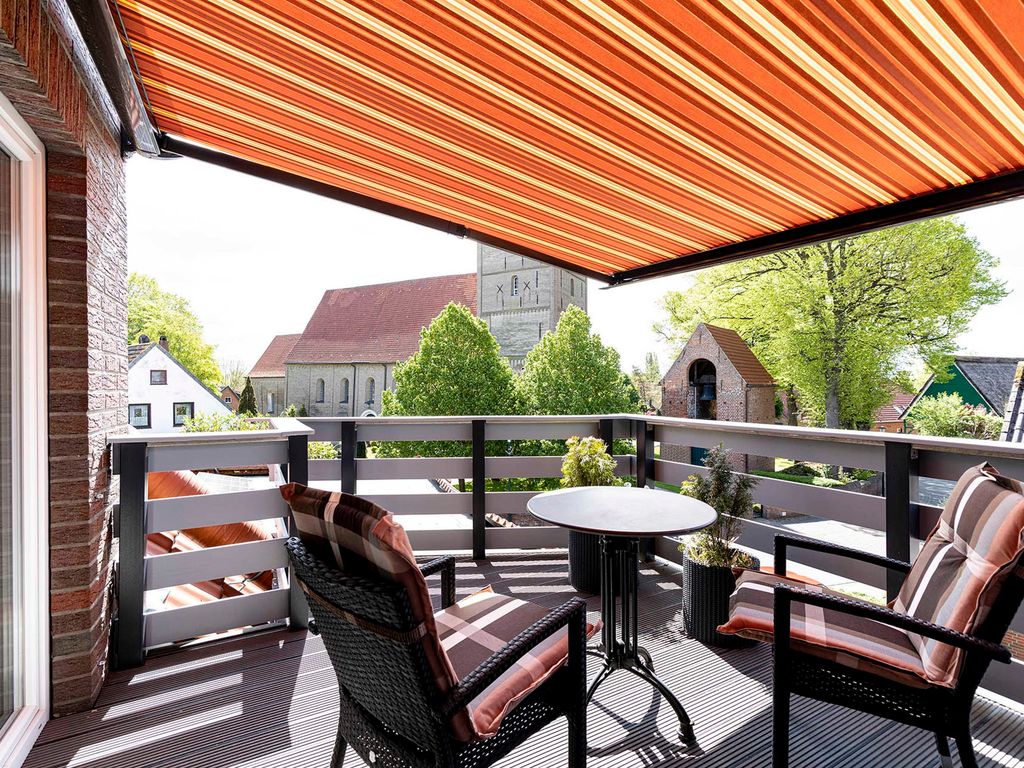 Südwest-Balkon mit Terrassenmöbel, elektrisch ausfahrbarer Markise und Blick auf die imposante Dorfkirche