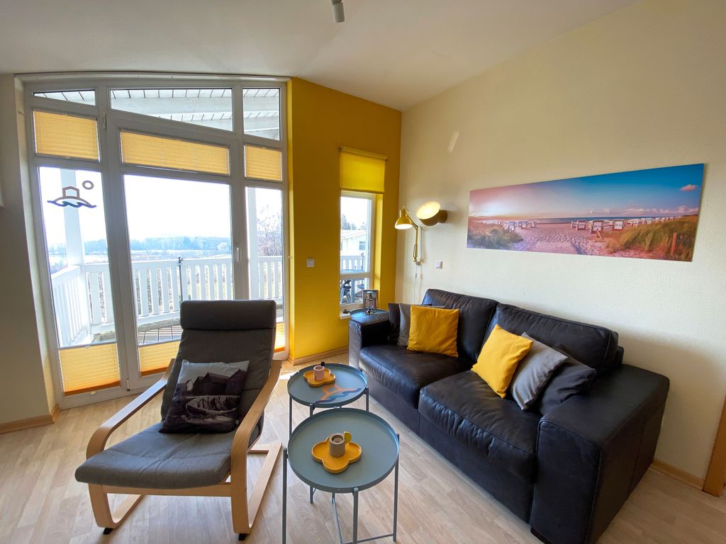 Haus Rügenscher Bodden Göhren – heller Wohnraum mit Sofa, Sessel und Tür zum Balkon