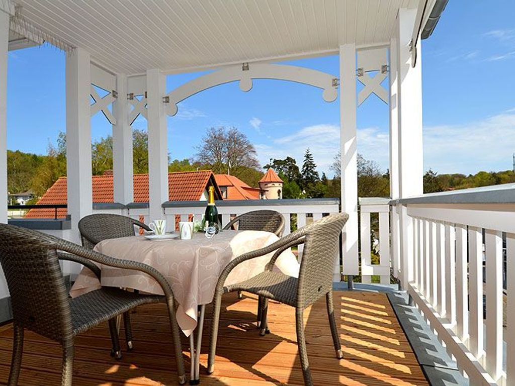 Villa Annika Sellin – überdachte Loggia mit Sitzgruppe unter der weißen Holzverzierung und Blick über die Dächer Sellins