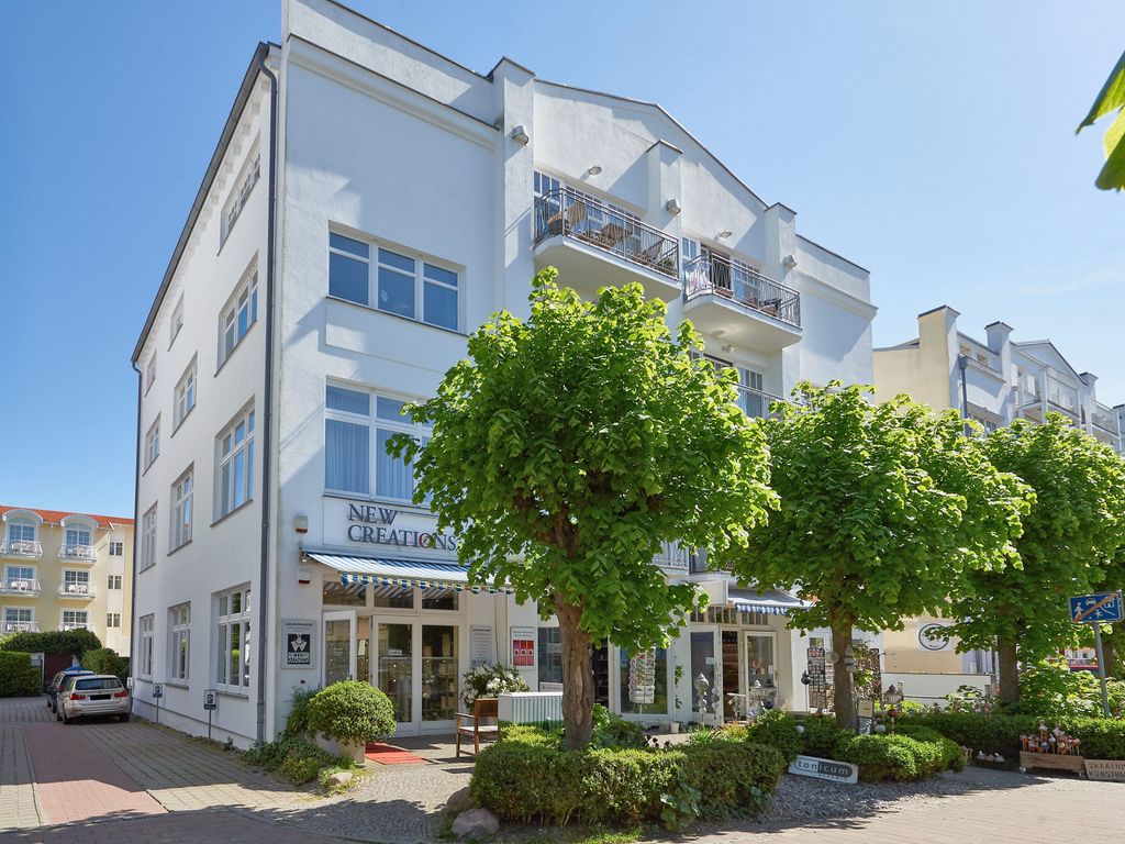 Haus Jahreszeiten Binz: weißes Appartementhaus mit Balkonen und Ladenzeile in der Margaretenstraße