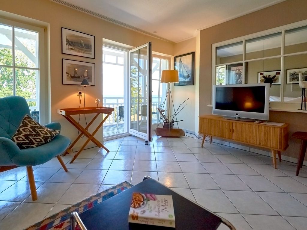 Seeschloss Binz – Wohnzimmer einer Ferienwohnung mit Sessel, TV und offener Balkontür zum Meer