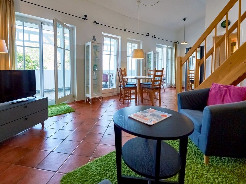 Seeschloss Binz – Wohn-Essbereich einer Maisonette-Ferienwohnung mit Holztreppe zur Galerie und Balkonfenstern