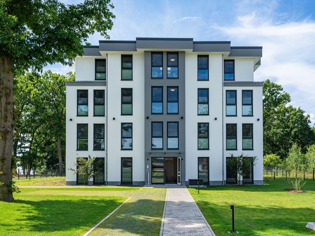 Oase am Haff – weißes Wohnhaus der Anlage mit Rasenfläche und altem Baumbestand