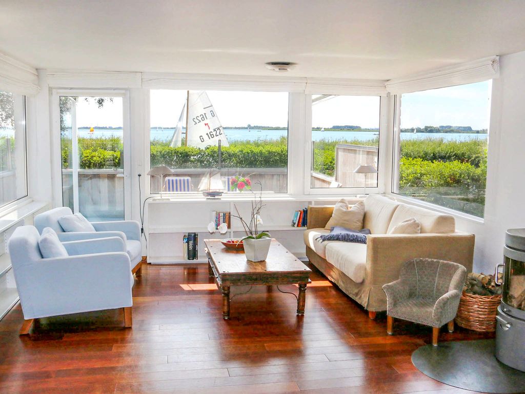 Lichtdurchflutetes Wohnzimmer mit großem Fensterfront, Kamin und Blick auf das Wasser  entspannter Rückzugsort mit maritimem Flair.