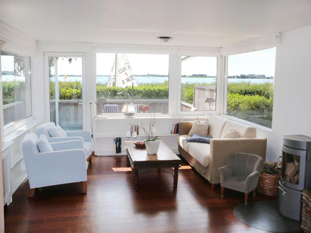 Lichtdurchflutetes Wohnzimmer mit großem Fensterfront, Kamin und Blick auf das Wasser  entspannter Rückzugsort mit maritimem Flair.