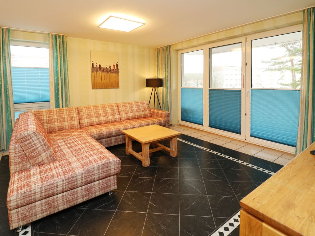 Gemütlicher Wohnbereich der Ferienwohnung Q05 im Quartier 18 mit großer Fensterfront und direktem Zugang zum Balkon zur Strandstraße.