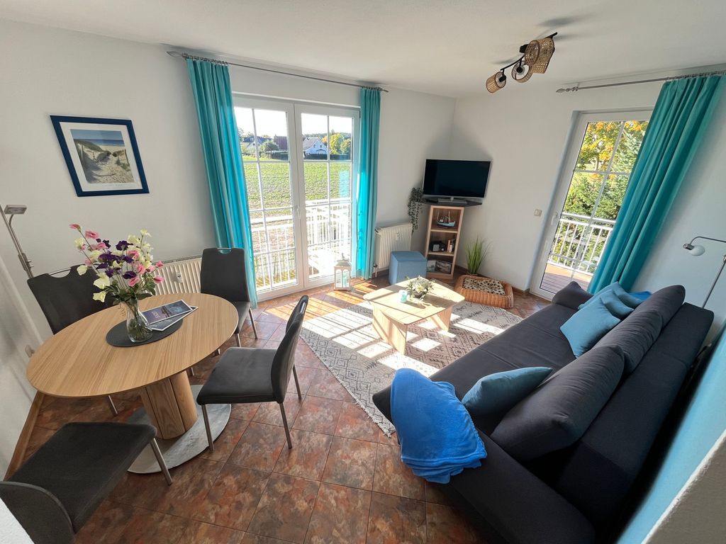 Wohnbereich mit Schlafcouch, offener Küche, Essplatz und Zugang zum Balkon