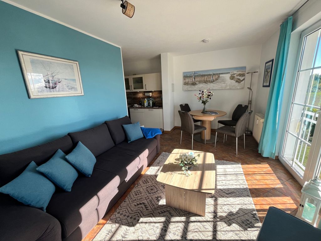Wohnbereich mit Schlafcouch, offener Küche, Essplatz und Zugang zum Balkon