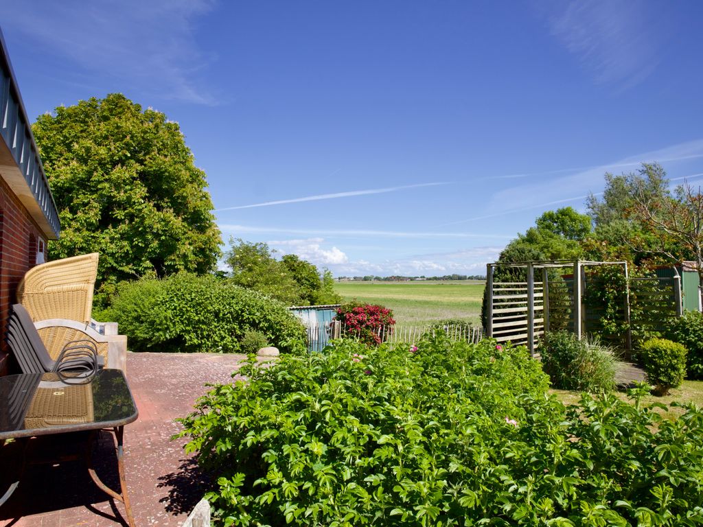 Ruhiges Reetdachhaus mit Strandkorb im Garten und Blick auf weite Felder