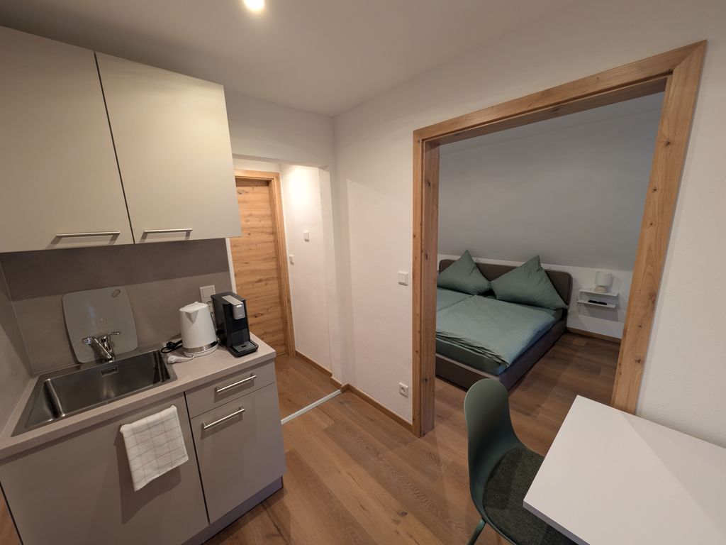 Zwischenraum mit Gang, Küchenzeile und Sitzgelegenheit. Zugang ins Schlafzimmer und Bad