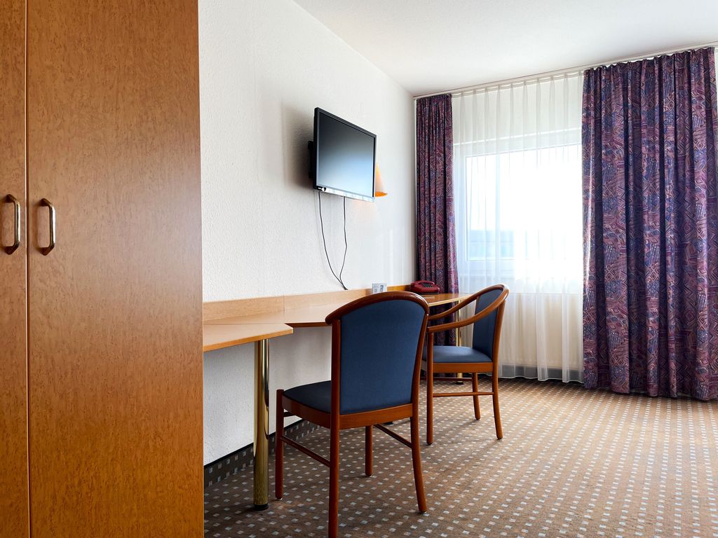Blick in das Einzelzimmer mit Schreibtisch, Kleiderschrank und TV