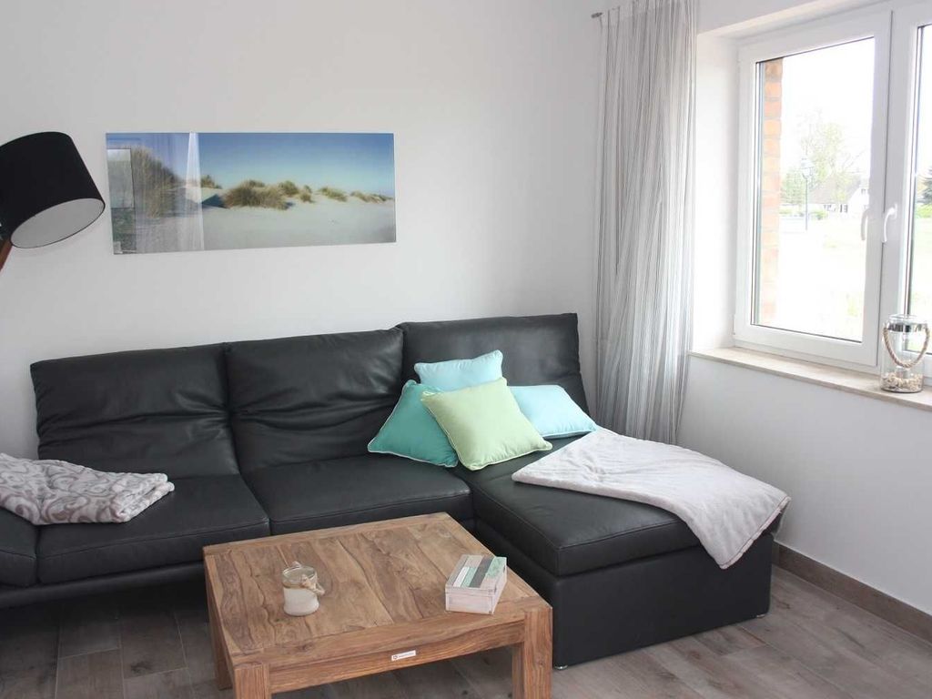 Das Ferienhaus Kormoran im Ostseebad Karlshagen auf der Insel Usedom zeigt ein helles Wohnzimmer mit Ledersitzgruppe, Couchtisch und Blick ins Freie.