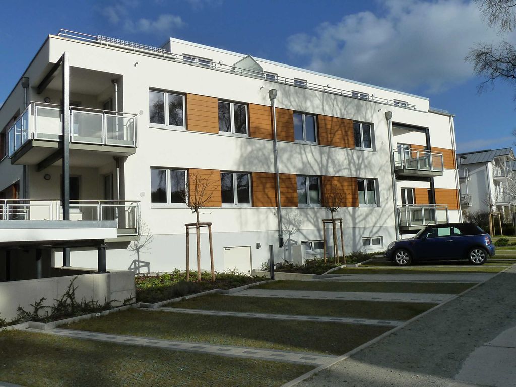 Strandhaus Juliusruh – moderne weiße Fassade mit Holzverkleidung, Glasbalkonen und Stellplätzen vor dem Haus