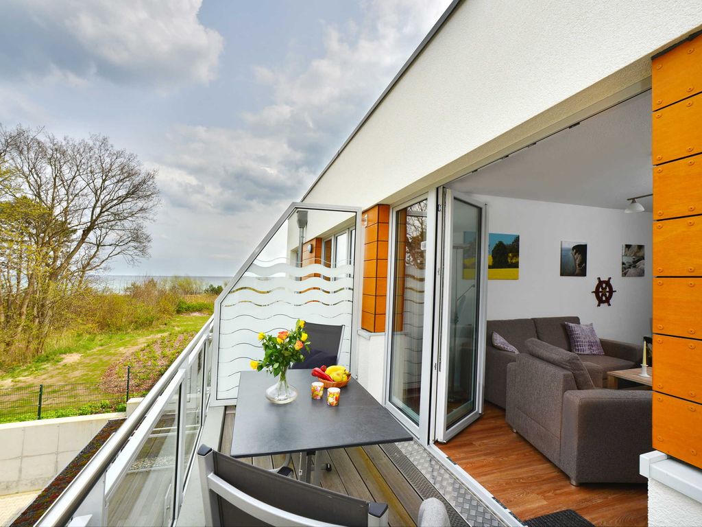 Strandhaus Juliusruh – Balkon mit Tisch, offene Balkontür zum Wohnzimmer, im Hintergrund die Ostsee
