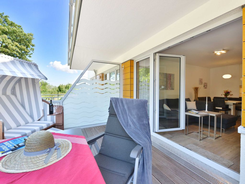 Strandhaus Juliusruh – Terrasse mit Strandkorb und Blick in den hellen Wohn-Essbereich einer Ferienwohnung